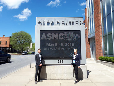 Ein Mann und eine Frau vor einer großen digitalen Veranstaltungsanzeige im Freien mit der Aufschrift "ASMC"